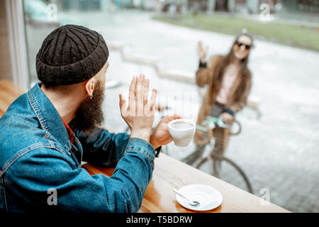 Elegante uomo incontro la sua fidanzata con biciclette mentre seduto con caffè vicino alla finestra presso il cafe Foto Stock