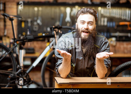 Ritratto di un bel allegro repairman in abbigliamento da lavoro in officina di biciclette Foto Stock