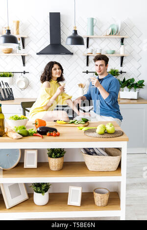 Giovani carino coppia - un ragazzo e una ragazza romanticamente trascorrere il tempo in cucina. Un paio di drink alcolici e prepara una insalata Foto Stock