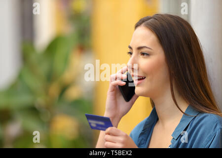 Compratore felice di parlare su smart phone tenendo la carta di credito in strada Foto Stock