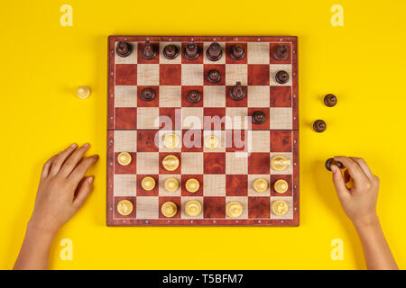 Il capretto con le mani su una scacchiera giocare a scacchi gioco su sfondo giallo Foto Stock