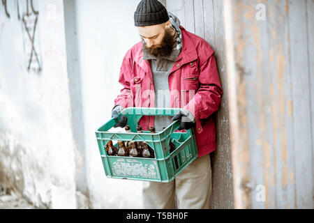 Senzatetto mendicante portando scatola con le bottiglie di vetro per il punto di raccolta. Modo di guadagnare denaro per i poveri Foto Stock