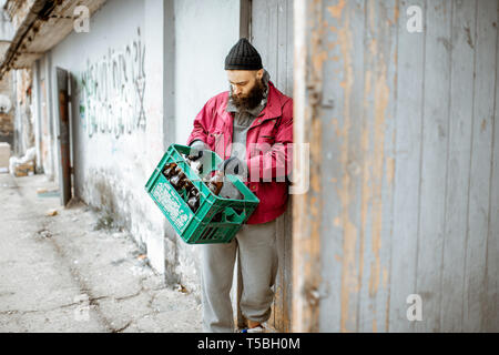 Senzatetto mendicante portando scatola con le bottiglie di vetro per il punto di raccolta. Modo di guadagnare denaro per i poveri Foto Stock