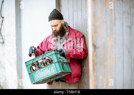 Senzatetto mendicante portando scatola con le bottiglie di vetro per il punto di raccolta. Modo di guadagnare denaro per i poveri Foto Stock