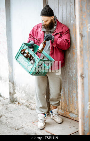 Senzatetto mendicante portando scatola con le bottiglie di vetro per il punto di raccolta. Modo di guadagnare denaro per i poveri Foto Stock