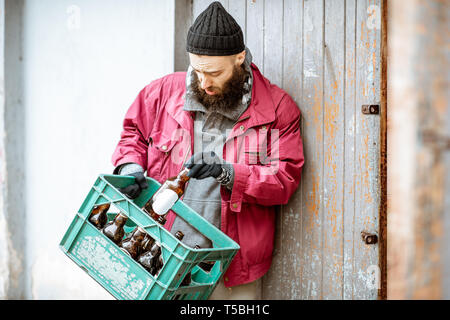 Senzatetto mendicante portando scatola con le bottiglie di vetro per il punto di raccolta. Modo di guadagnare denaro per i poveri Foto Stock