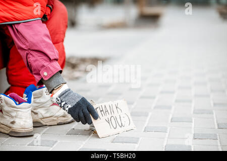 Mendicante chiede un po' di soldi con la coppa e la ringrazio cardboad sulla strada, vista da vicino Foto Stock