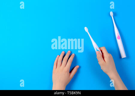 Kid le mani e gli spazzolini da denti elettrici su sfondo blu, vista dall'alto Foto Stock