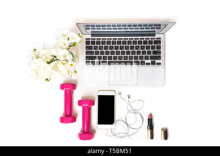 Donna area di lavoro con computer laptop notebook, attrezzature per il fitness rosa manubri, specchio cosmetico, telefono cellulare, cuffie e fiore bianco su sfondo bianco. Foto Stock