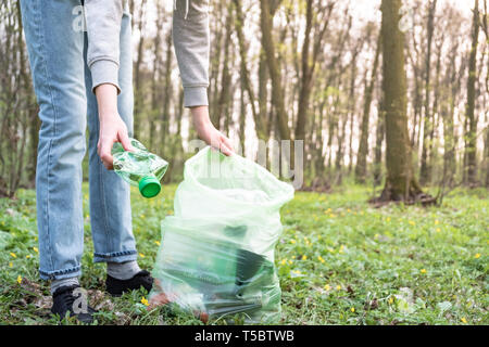 Pulizia-fino alla foresta di immondizia di plastica. Persona preleva una bottiglia di plastica nei boschi, concetto di consapevolezza in plastica attivismo. Foto Stock