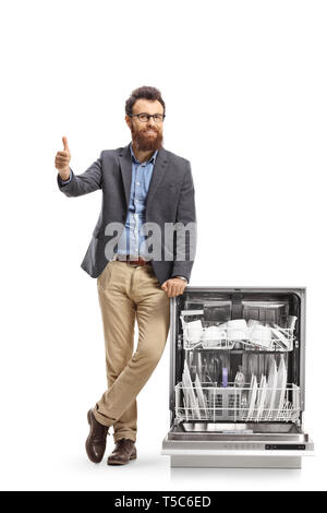 A piena lunghezza Ritratto di un giovane uomo barbuto in posa accanto a una lavastoviglie caricato e dando pollice in alto isolato su sfondo bianco Foto Stock