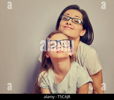 Smorfie sorridendo positivo casual madre cercando seduto con il suo infelice offeso pensando kid ragazza sulla parete viola sfondo. Famiglia di moda eye Foto Stock