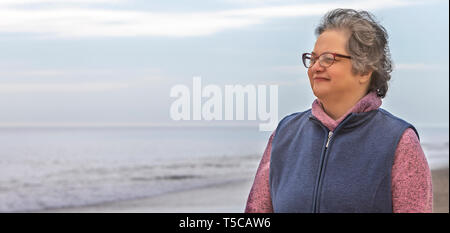 Un senior donna godendo di camminare nella sabbia sulla spiaggia dalla Ocean Shore. Foto Stock