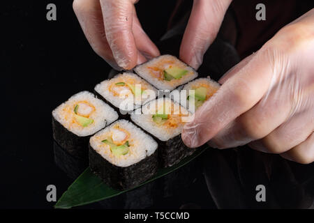 Lo chef prepara le mani il cibo giapponese, chef rendendo il sushi, preparazione di rotoli di Sushi con gamberi su sfondo nero Foto Stock