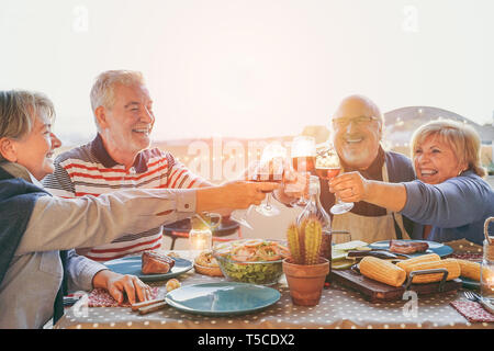 Felice senior amici divertendosi tifo con un bicchiere di vino rosso al barbecue in terrazza outdoor - persone mature di preparare la cena gli occhiali di tostatura Foto Stock
