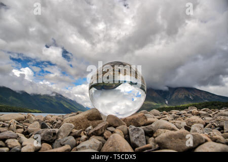 Sfera di cristallo seduto su ciottoli in corrispondenza del bordo del lago Foto Stock