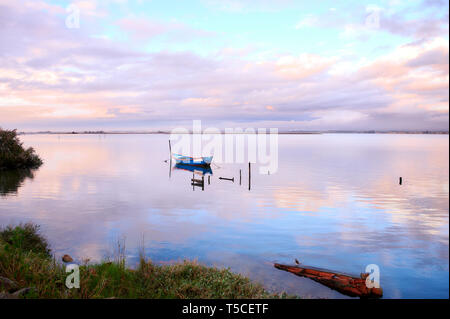 Unica barca legato ad un palo nel mezzo della laguna di Aveiro a Torreira. La rosa e arancione tramonto inverno nuvole riflettono in corrispondenza della superficie del lago. Foto Stock