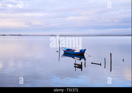 Unica barca legato ad un palo nel mezzo della laguna di Aveiro a Torreira. La rosa e arancione tramonto inverno nuvole riflettono in corrispondenza della superficie del lago. Foto Stock