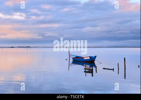 Unica barca legato ad un palo nel mezzo della laguna di Aveiro a Torreira. La rosa e arancione tramonto inverno nuvole riflettono in corrispondenza della superficie del lago. Foto Stock