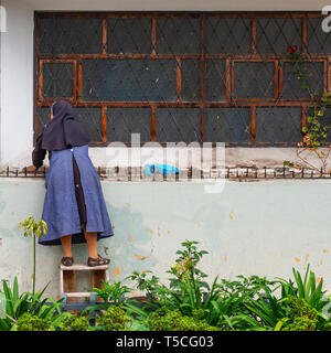 Square fotografia di una suora cattolica abito con la pulizia della parte esterna di un convento nel centro della città di Cuenca, Ecuador. Foto Stock