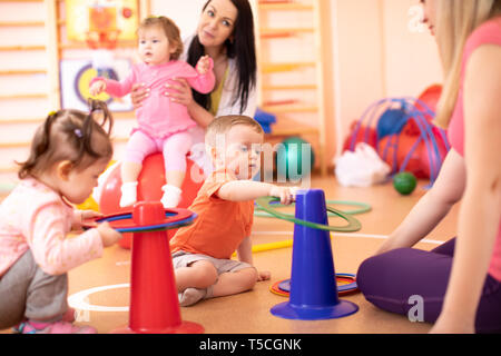 I bambini con le loro madri hanno divertimento in asilo nido palestra Foto Stock