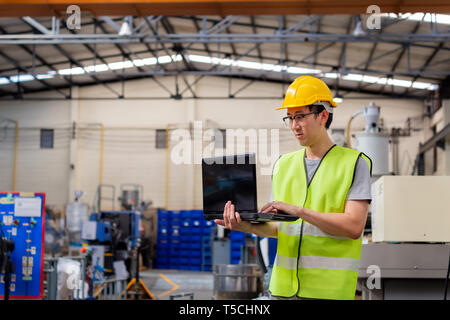 Asian maschio ingegnere industriale in hardhat lavora con il computer portatile in giacca di sicurezza alla fabbrica di fabbricazione. Lavorazione di stampaggio a iniezione in plastica industria Foto Stock