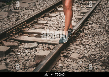 Gambe femmina in sneakers sul binario della linea ferroviaria Foto Stock