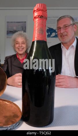 23 aprile 2019, Sassonia-Anhalt, Nebra: il sindaco di Nebra, Antje Scheschinski e Mike Eberle, managing director di Rotkäppchen Sektkellerei, sedersi davanti ad una vecchia bottiglia di vino spumante e time capsule di un sito in costruzione nella sala della comunità. Il 24.08.2018 la capsula è stata trovata durante i lavori di costruzione di un ponte Unstrut in Nebra che è stato inaugurato nel 1886. All'interno, c'era una bottiglia di champagne del marchio "Kloss & Foerster' - il precursore di Little Red Riding Hood - tra gli altri testimoni contemporanei. La cantina spumante ha acquisito la bottiglia per il suo archivio, il mo Foto Stock