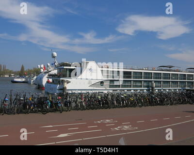 Una lunga fila di biciclette parcheggiate sulla banchina vicino alla stazione centrale di Amsterdam, con imbarcazioni da fiume in background e le piste ciclabili alla ribalta Foto Stock