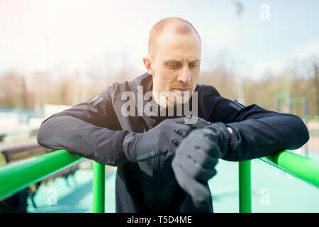 Foto del giovane atleta guardando a guardare mentre tirando verso l'alto sul verde della barra orizzontale Foto Stock
