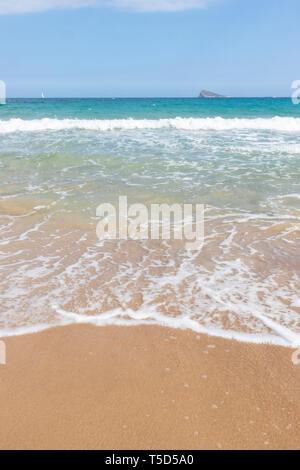 Ampio angolo di visione di onda spiaggia di lappatura con isola in background Alicante Spagna Foto Stock