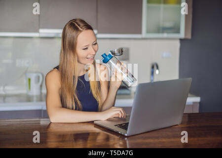 Ragazza assetata beve l'acqua, utilizza il computer portatile per il blogging in reti, orologi film, collegato a internet wireless. La donna legge notizie sul sito web Foto Stock