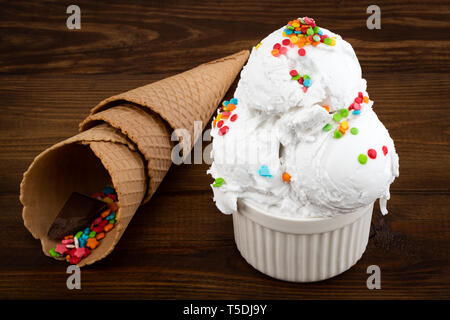 Piastra del gelato alla vaniglia scoop cambia spruzza e waffle rocche su sfondo di legno. Foto Stock