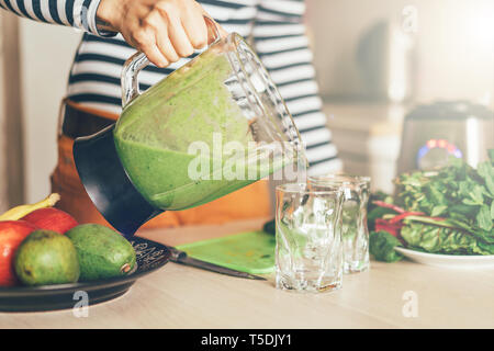 Donna di colata a mano frullato di verde in un bicchiere Foto Stock