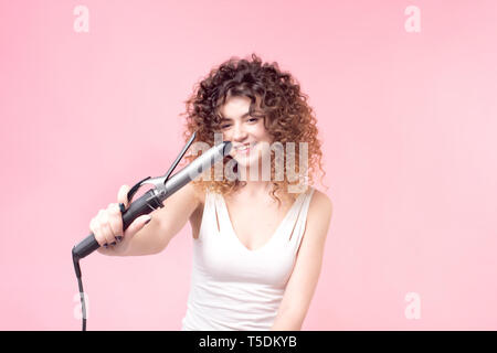 Affascinante ragazza con un sorriso sul suo viso capelli ricci in una T-shirt bianca con arricciacapelli Foto Stock