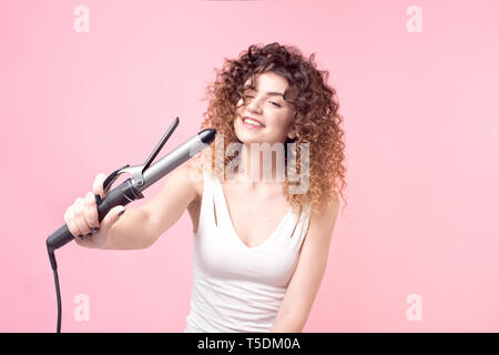 Affascinante ragazza con un sorriso sul suo viso capelli ricci in una T-shirt bianca con arricciacapelli Foto Stock