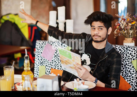 Barba uomo asiatico in abbigliamento casual seduta indoor cafe, leggere il menu e chiamata cameriere. Foto Stock