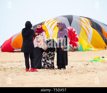 Quattro donne Musulmane di indossare il hijab come scattare foto sulla spiaggia in il conservatore Kelantan Stato della Malaysia. In fondo è un grande aquilone sgonfio. Foto Stock