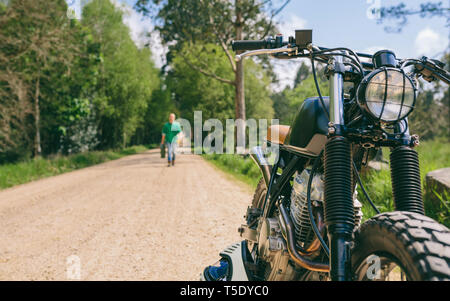 Custom vintage moto sul lato della strada con guy in background a piedi con benzina può Foto Stock