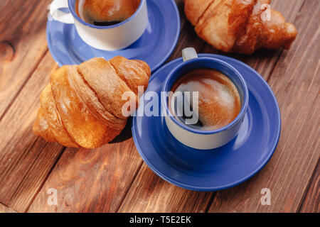 Due tazze di caffè caldo e cornetti su uno sfondo di legno, buona illuminazione, atmosfera mattutina Foto Stock