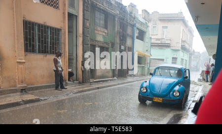 HAVANA CUBA - luglio 8 2012; Heavy Rain in strada di l'Avana su un blu brillante VW Beetle auto mentre la gente shelter o sostare sotto la pioggia. Foto Stock