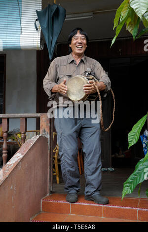 Uomo Bidayuh suonare il tamburo sul portico di casa, Kampung Annah Rais, Sarawak (Borneo), Malaysia Foto Stock