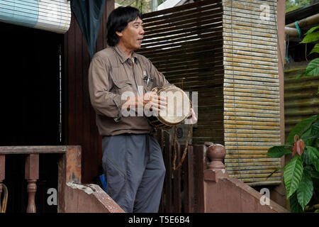 Uomo Bidayuh suonare il tamburo sul portico di casa, Kampung Annah Rais, Sarawak (Borneo), Malaysia Foto Stock