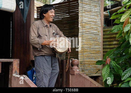 Uomo Bidayuh suonare il tamburo sul portico di casa, Kampung Annah Rais, Sarawak (Borneo), Malaysia Foto Stock