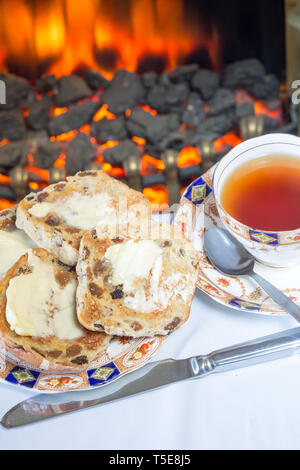 Tostato caldo imburrato cross panini serviti per la lingua inglese high tea su un osso di cina la piastra con una tazza di tè inglese. Foto Stock