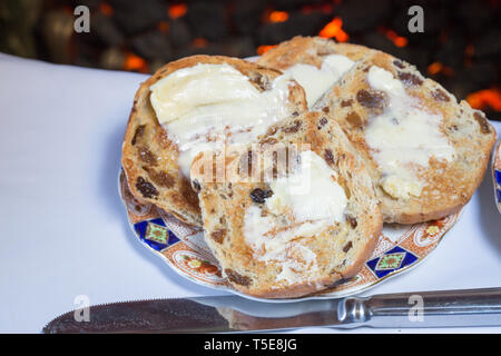 Tostato caldo imburrato cross panini serviti per la lingua inglese high tea su un osso di cina la piastra con una tazza di tè inglese. Foto Stock