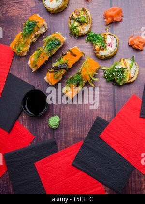 Tabella servita con sushi su sfondo scuro. Rotoli di sushi, wakame, zenzero, wasabi Overhead, tradizionale cibo giapponese Foto Stock