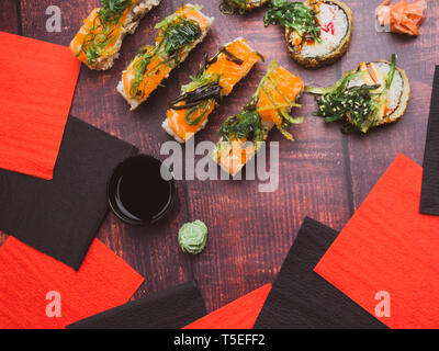 Vista dall'alto di piatti giapponesi su sfondo scuro. Sushi di salmone, sushi rotoli a bordo, carne di granchio, gamberetti, wakame, lo zenzero, la superficie in legno Foto Stock