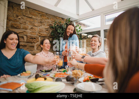 Piccolo gruppo di amici di sesso femminile preparare un pranzo sano all'interno di un conservatorio in un fine settimana di distanza. Essi stanno facendo un celebrativo Foto Stock