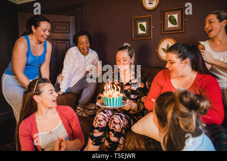 Piccolo gruppo di amiche per festeggiare un compleanno con una torta di compleanno durante i momenti di relax a casa. Foto Stock